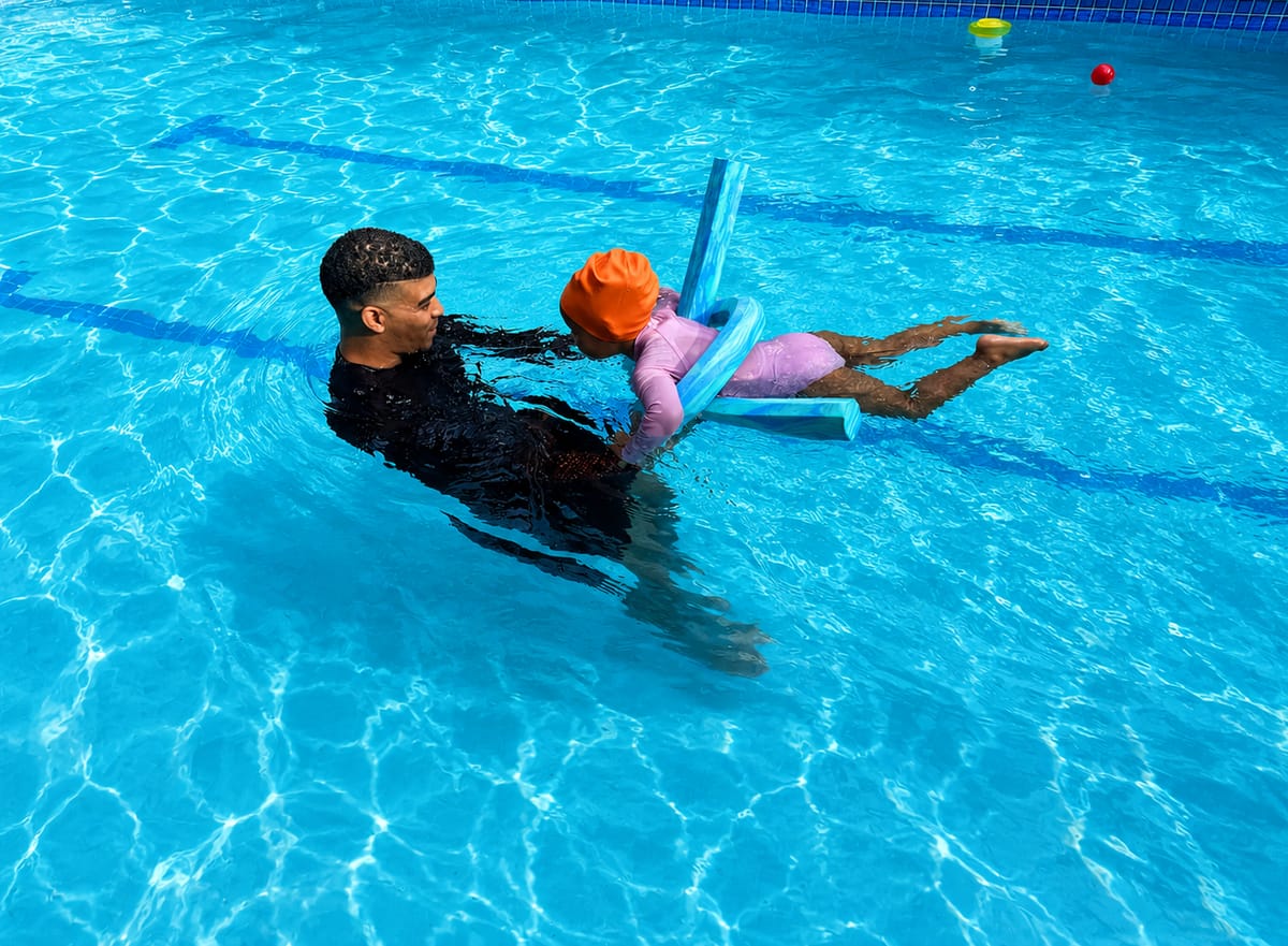 Instructor supporting a young child on a pool noodle during a back float and kick drill