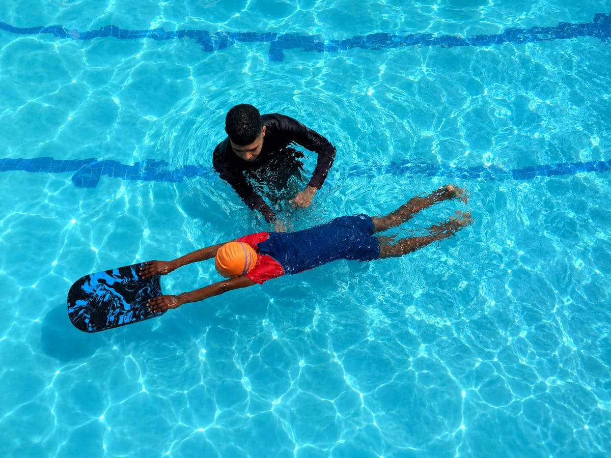 Instructor guiding a child kicking on a kickboard while learning to swim