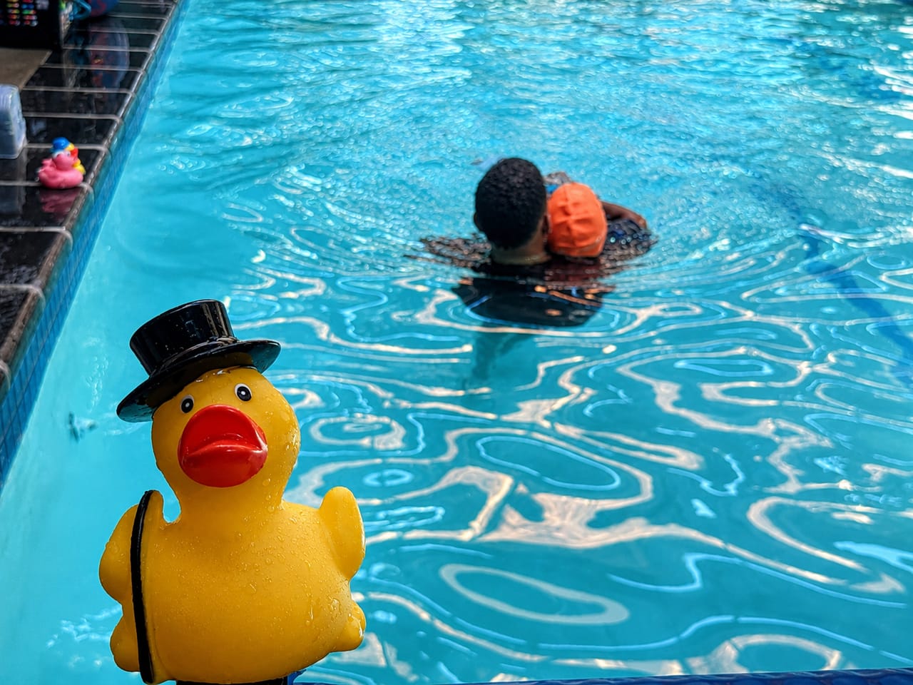 A child swimming in the heated indoor pool, with a top-hat rubber duck on the poolside