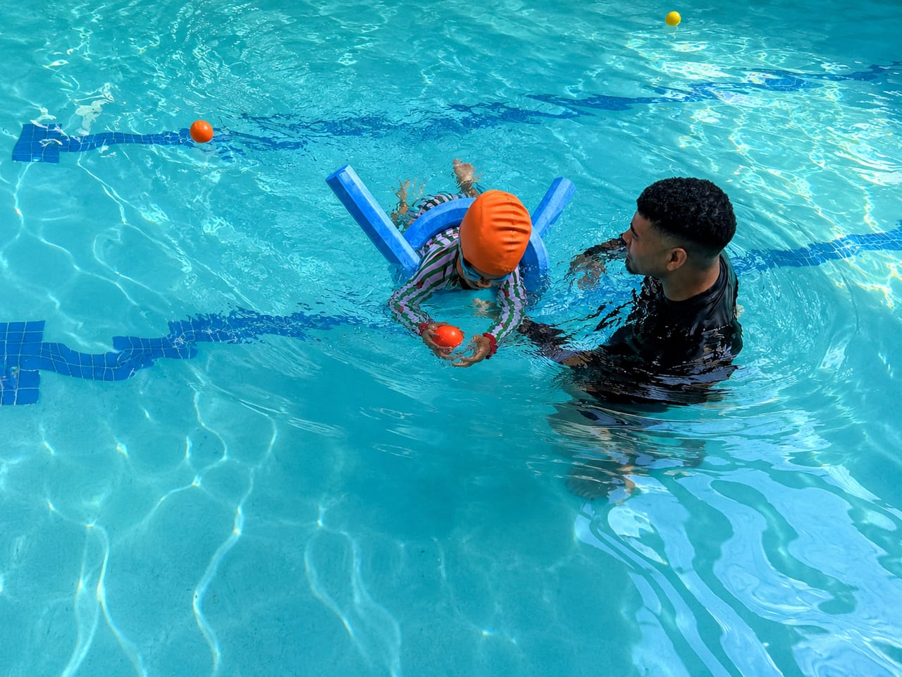 Instructor guiding a child balancing on a pool noodle during a float drill