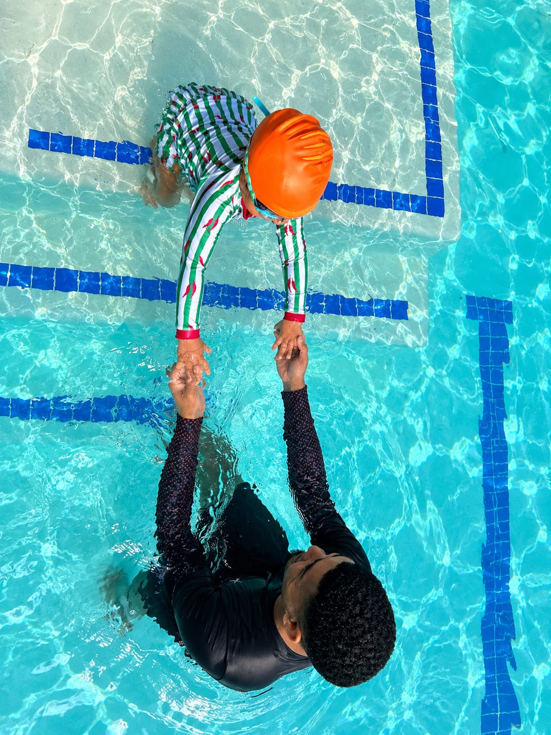 Overhead view of an instructor holding a child's hands at the pool steps