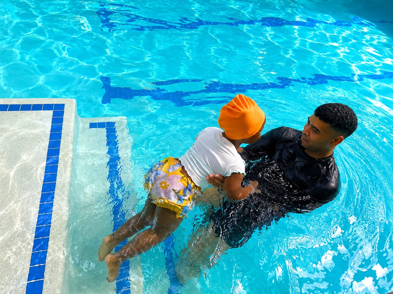 Instructor gently supporting a toddler entering the water at the steps