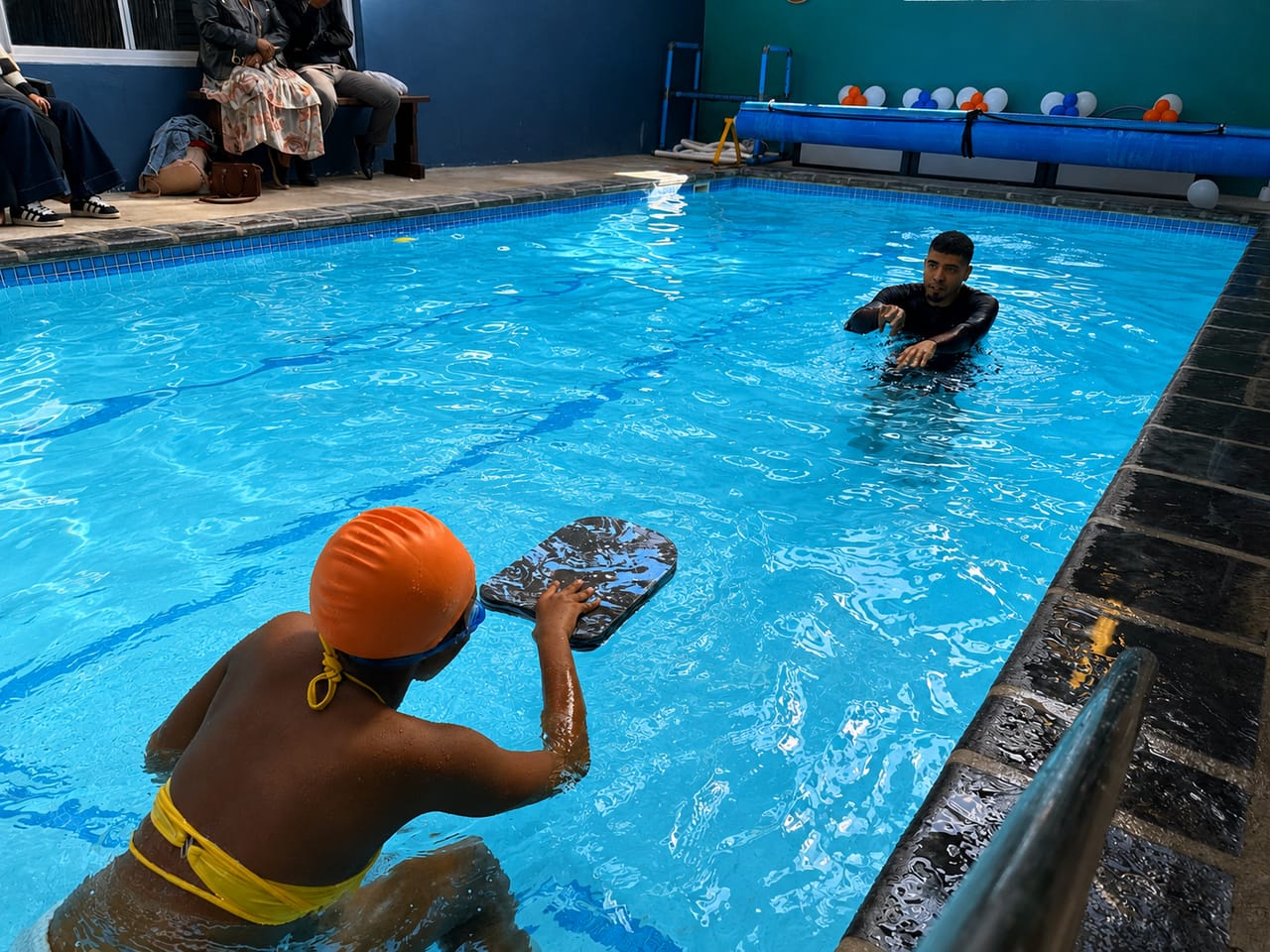 A child with a kickboard preparing to push off toward the instructor across the pool