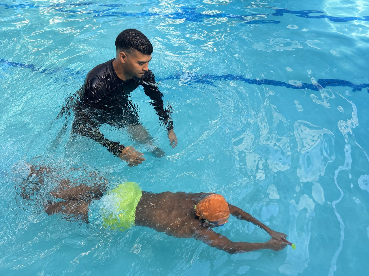 Instructor coaching a child swimming freestyle and reaching for a toy