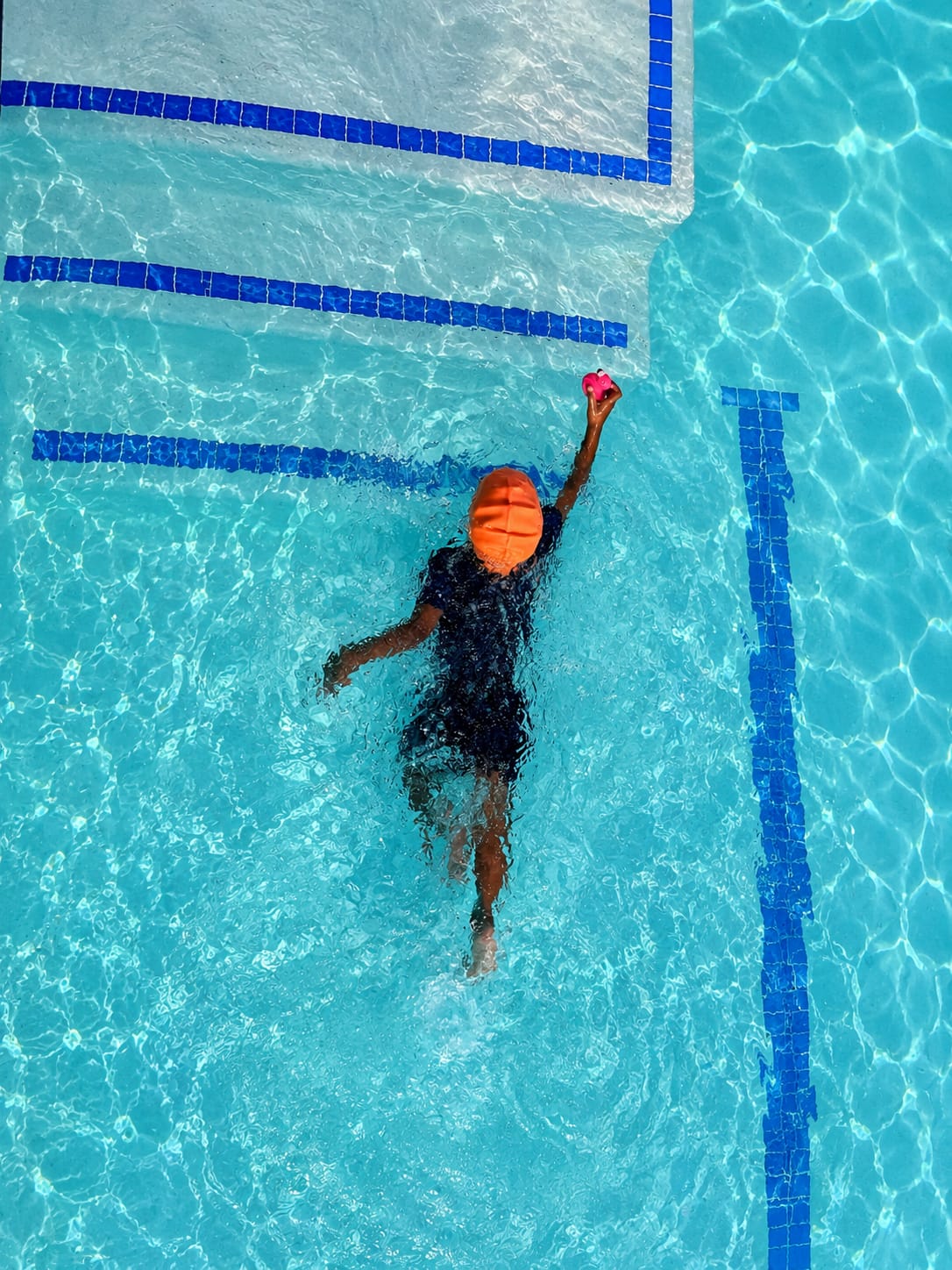 Overhead view of a child swimming confidently across the pool toward a toy