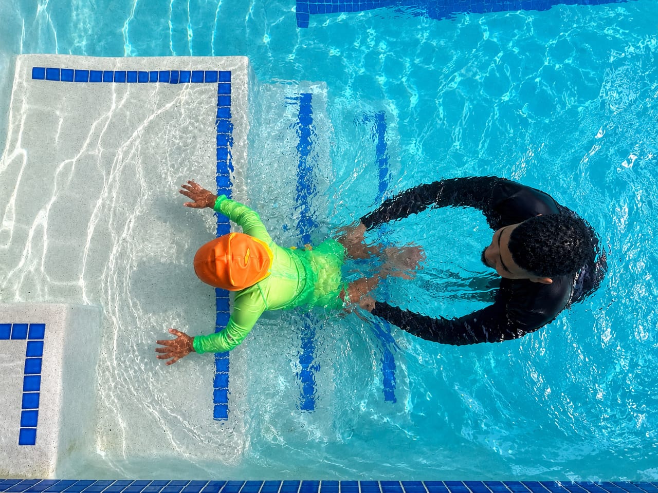 Overhead view of a child on the pool steps with the instructor close by