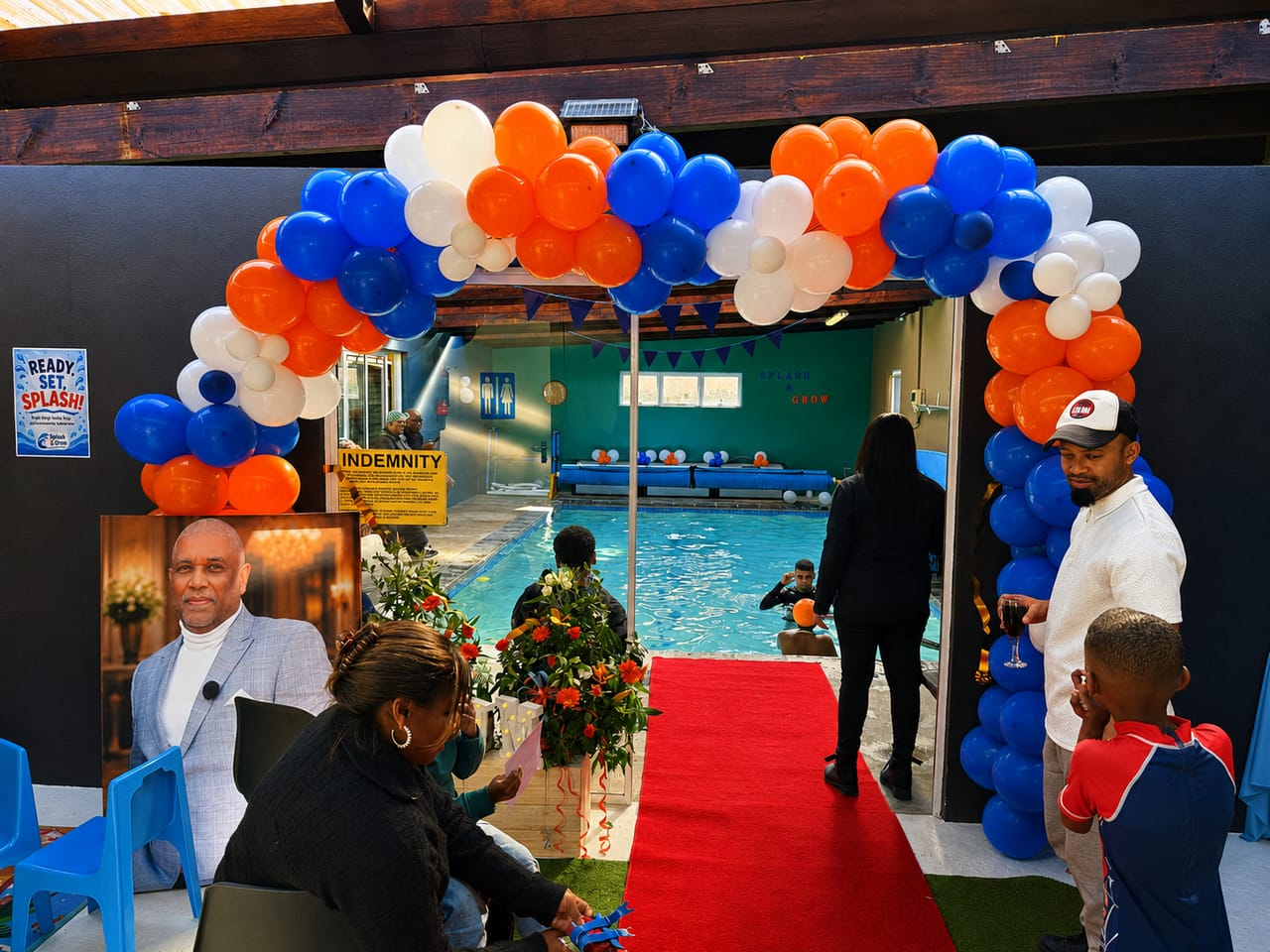 Open day entrance with a blue, orange and white balloon arch and red carpet leading to the heated indoor pool