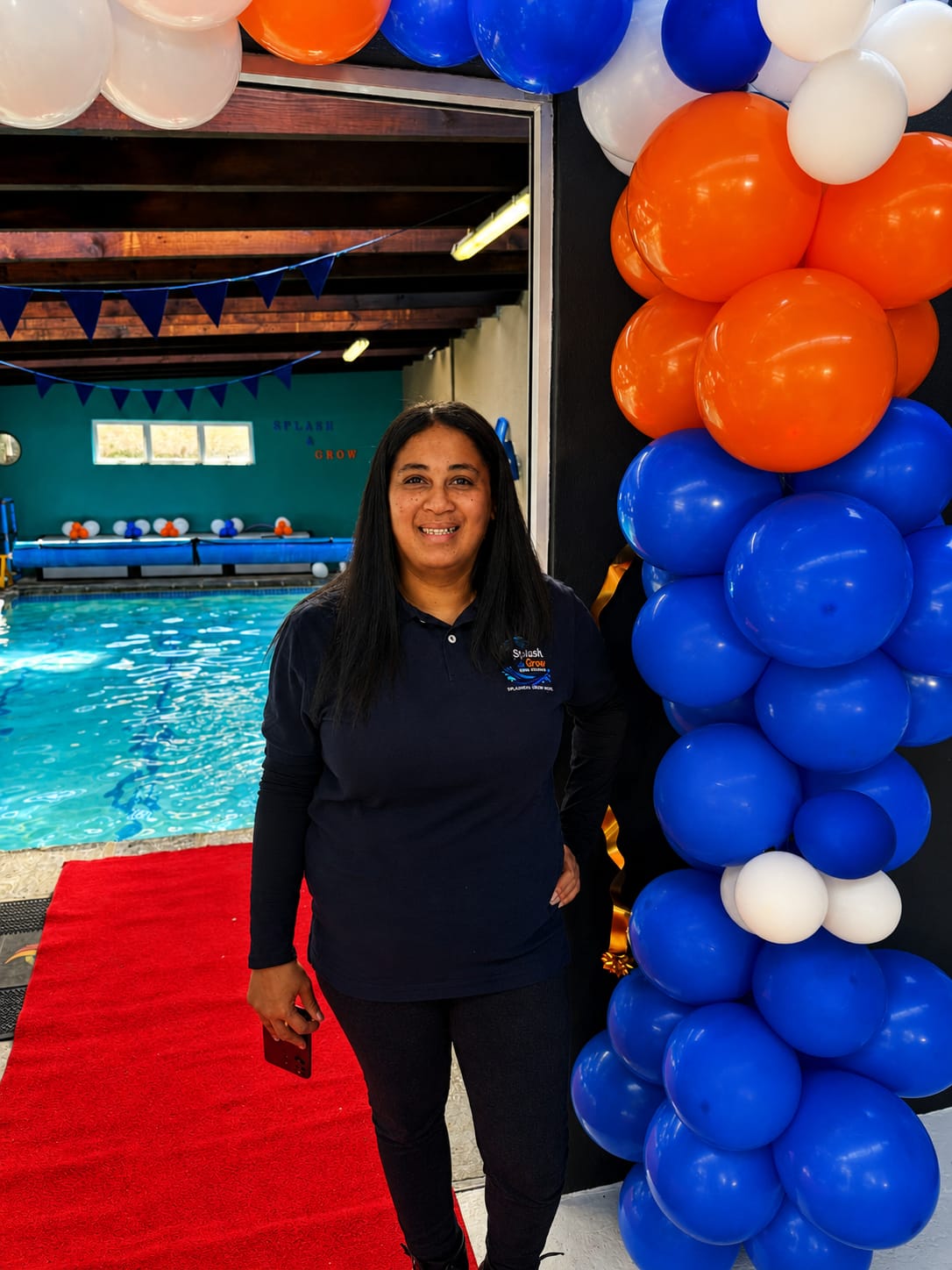 A Splash & Grow team member beside a balloon column at the indoor pool entrance during the open day