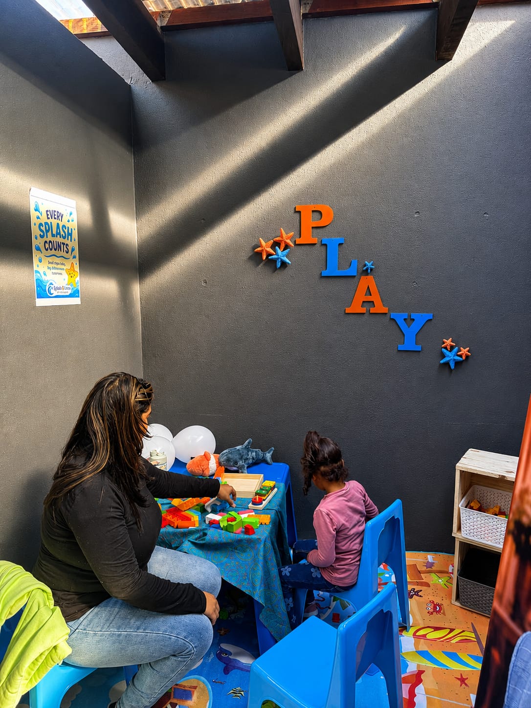 A parent and child playing at a table in the children's play area, decorated with PLAY lettering
