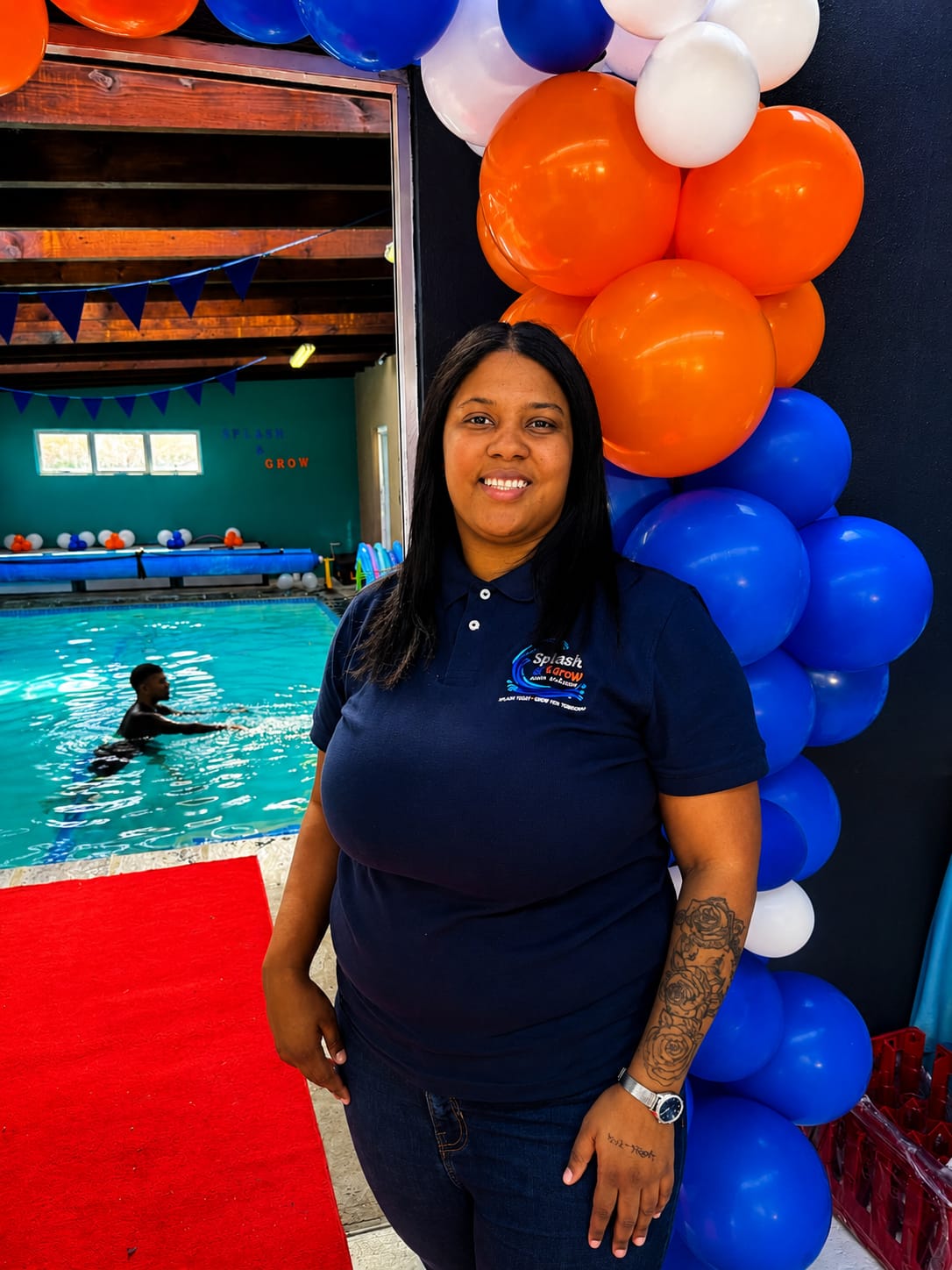 A Splash & Grow team member by the heated pool with a child swimming, decorated with open day balloons